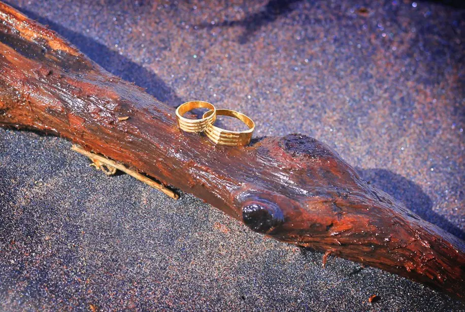 Close-up of the couple’s wedding rings with sand in the background