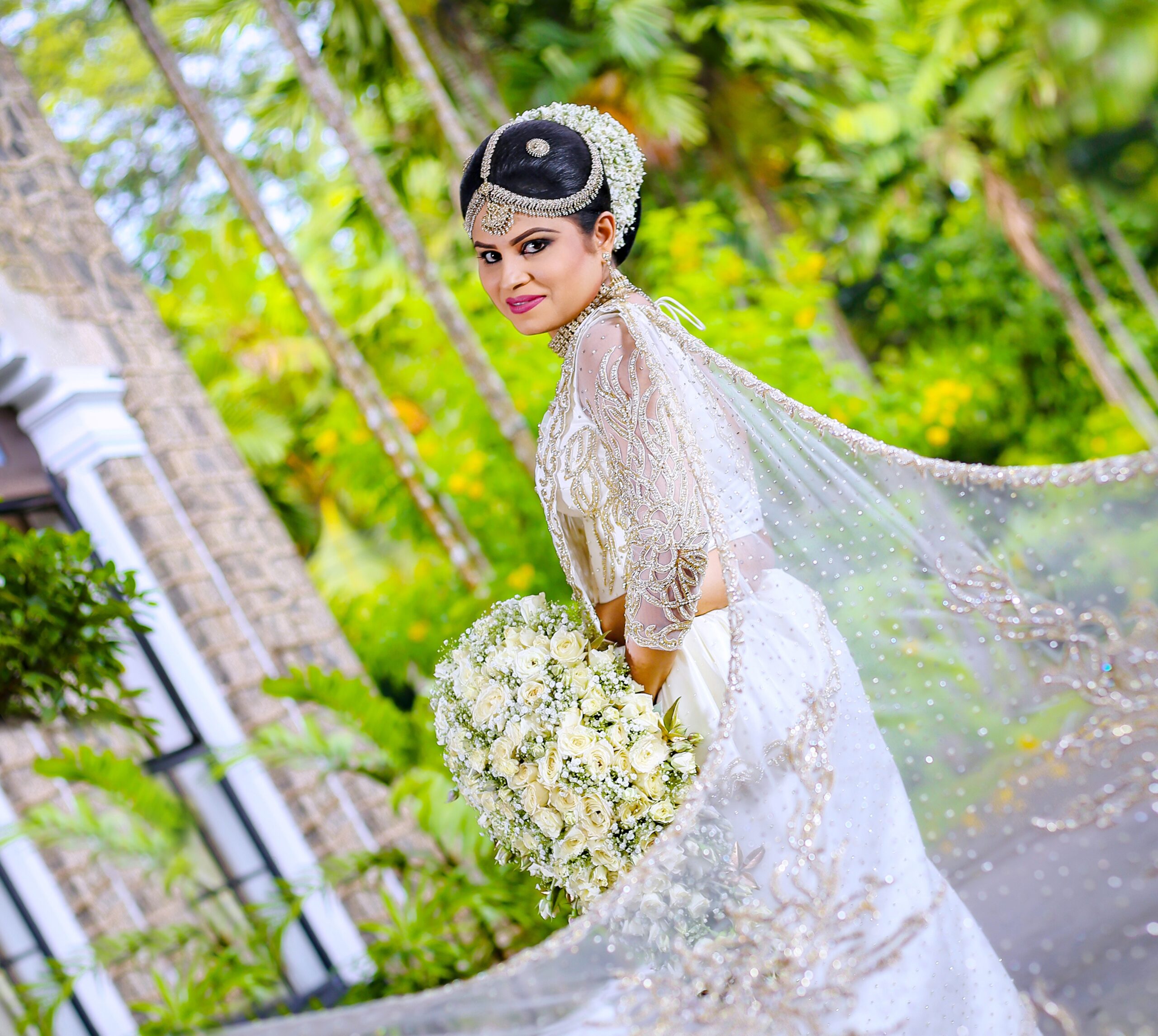 Bride in white saree standing among lush greenery