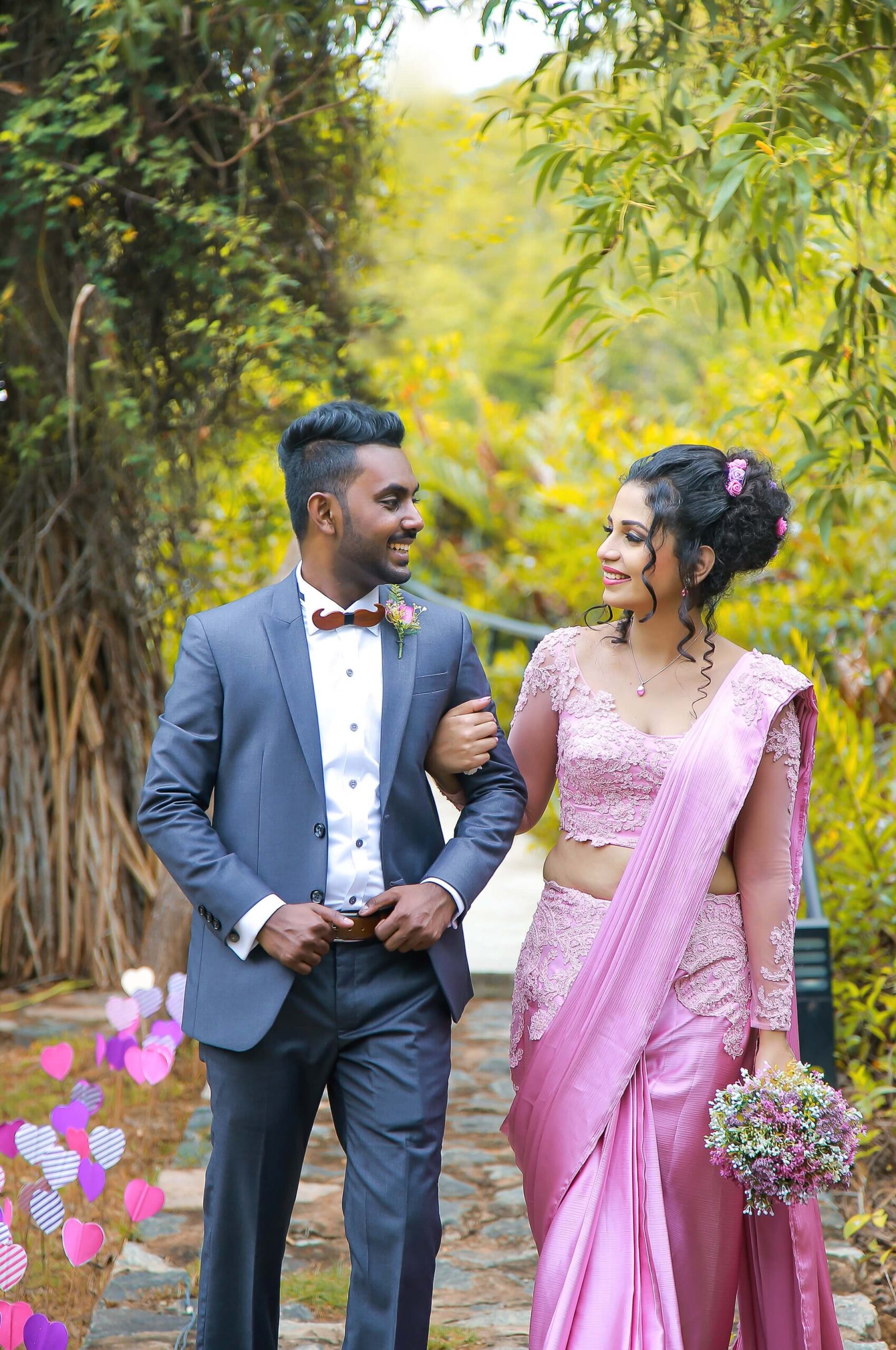 Bride and groom walking together in a lush green outdoor setting.